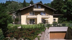 Ein zweistöckiges Haus mit Balkon, Garage und Garten mit verschiedenen Pflanzen und Blumen.