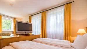 Ein Hotelzimmer mit zwei Betten, einem Fernseher auf einem Holztisch und einem Fenster mit gelben Vorhängen.