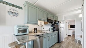 A kitchen with light blue cabinets, a built-in oven, a microwave, and a refrigerator. There is a wooden countertop and a sink.