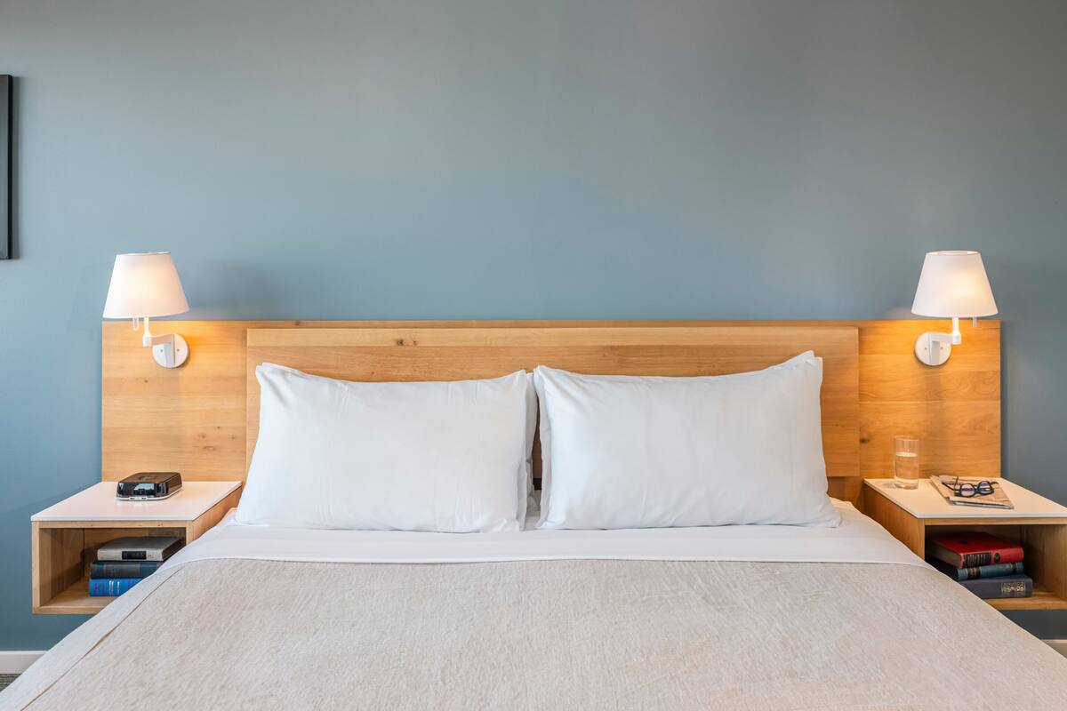 A neatly made bed with white linens, two bedside tables with lamps, and a wooden headboard.