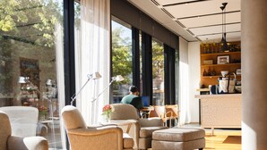 Et moderne interiør med store vinduer, et siddeområde med lænestole og skærmer samt en disk med diverse ting.