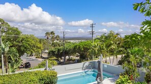 Una piscina rodeada de exuberante vegetación, cielo despejado y una vista distante de edificios.