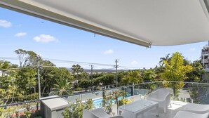 A balcony with a pool, white furniture, and a view of a cityscape and mountains.