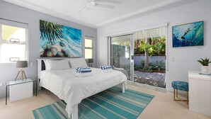 A modern bedroom with a bed, a glass door leading to a garden, and two paintings on the walls.