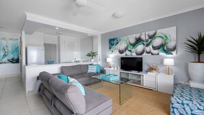 A modern living room with a grey sofa, a glass coffee table, a flat-screen TV, and abstract art on the wall.