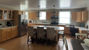 A modern kitchen with wooden cabinets, a central island with chairs, a refrigerator, stove, and a microwave. - Located in the heart of Downtown Saugatuck (Saugatuck)