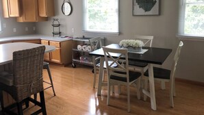 A kitchen with wooden cabinets, a dining table with white chairs, and a window with blinds. - Located in the heart of Downtown Saugatuck (Saugatuck)