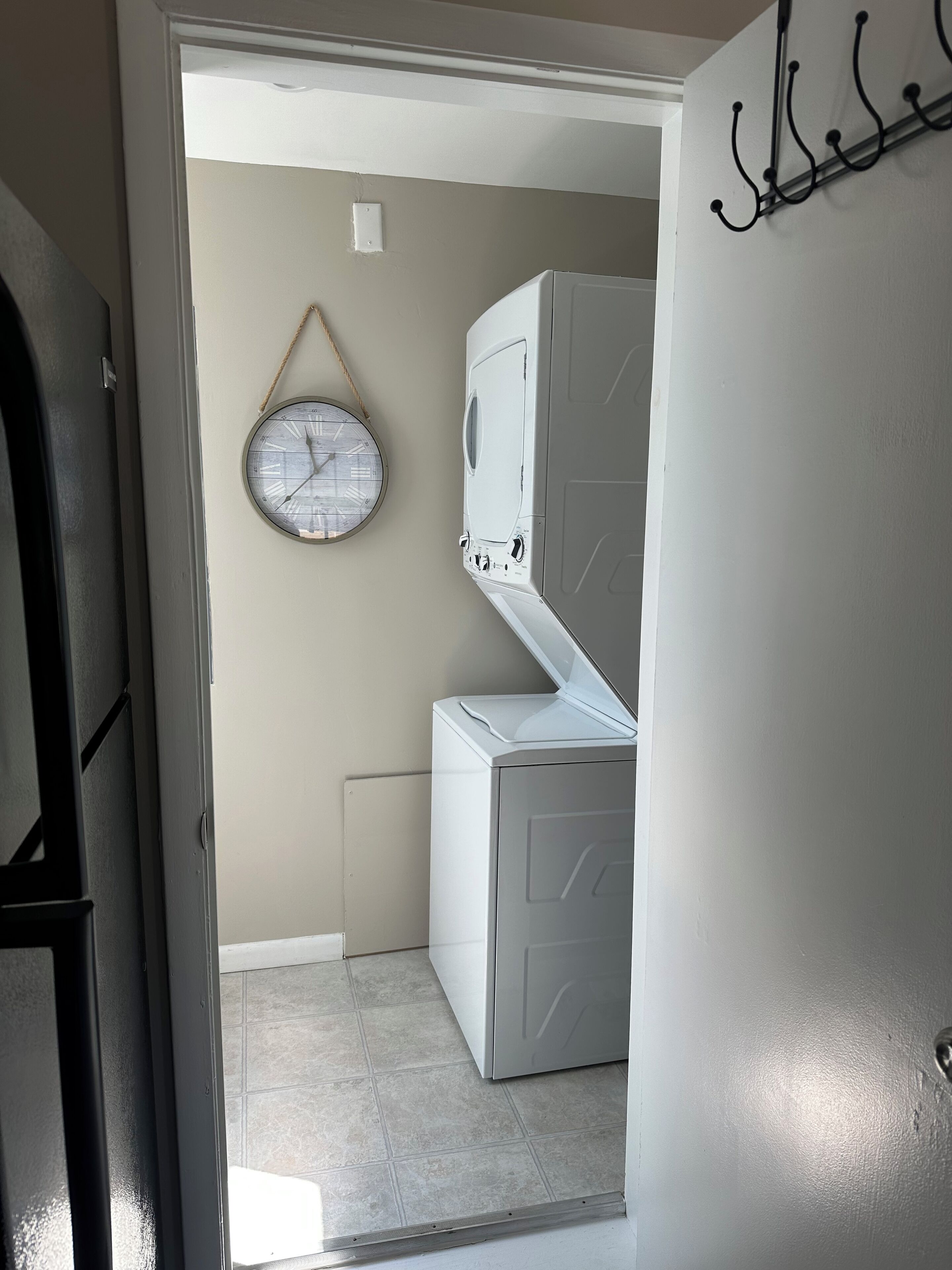 A laundry room with a washing machine and dryer, a clock on the wall, and a door with a coat rack.