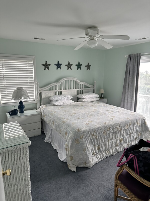 Un dormitorio con cama blanca, ventilador de techo, mesita de noche con lámpara y decoración de estrellas en la pared.