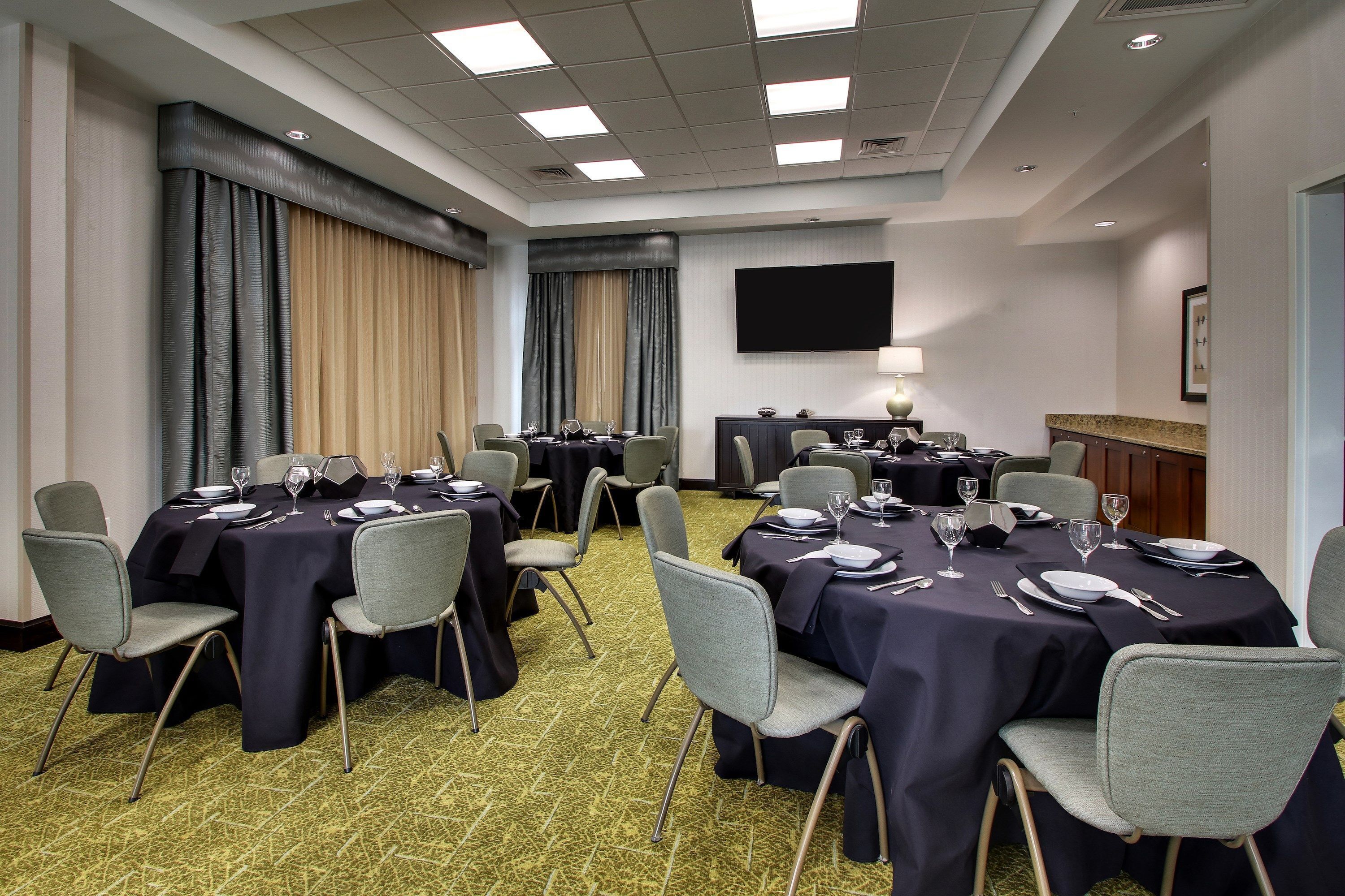 Un salón de conferencias con varias mesas dispuestas para comer, equipado con sillas y cubertería.