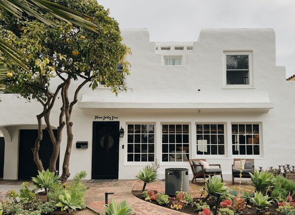Un bâtiment blanc avec une porte noire, une enseigne indiquant « Three Forty Five », et un jardin avec différentes plantes.