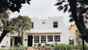 A white two-story house with a black door, numbered 345, and a garden with various plants and a pathway leading to the entrance.