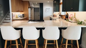 A modern kitchen with a central island, wooden chairs, and dark cabinetry.