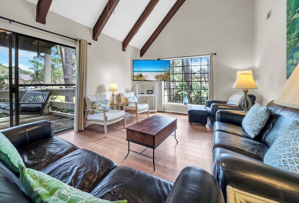 A spacious living room with leather sofas, a wooden coffee table, and large windows offering a view of the outdoors.