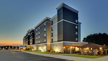 A multi-story hotel with a modern design, featuring a parking lot and outdoor seating area.