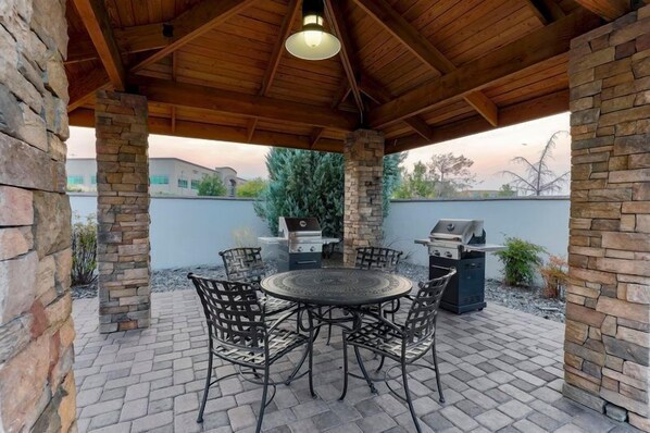 An outdoor patio with a round table and chairs, a grill, and stone pillars. - Accessible 1BR Suite w/ Free Breakfast & Pool Reno (Reno)