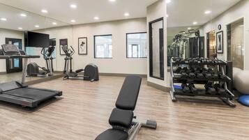A gym with exercise equipment, a treadmill, a bench, and a mirror wall.