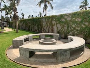Relax in a serene, communal seating area surrounded by lush greenery and a central fire pit.