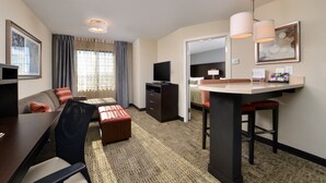 A hotel room with a dining area, a sofa, a TV, and a desk with a lamp.