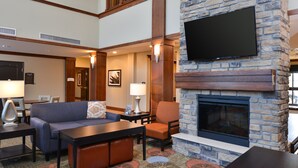 A hotel lobby with a stone fireplace, a flat-screen TV mounted on the wall, a sofa, a chair, and a coffee table.