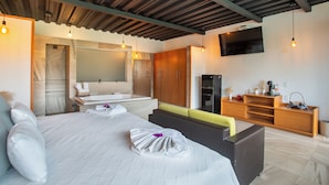 Una habitación de hotel moderna con una cama grande, un baño con bañera, muebles de madera y un televisor de pantalla plana.