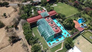 Vista aérea de un complejo turístico con una piscina grande, varias habitaciones para huéspedes y un jardín ajardinado.