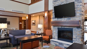 A hotel lobby with a stone fireplace, a flat-screen TV mounted on the wall, a sofa, a chair, and a coffee table. - Cozy Suite in Rochester | Free Breakfast + Shared Pool & Hot Tub. Near Mayo Clinic! (Rochester)