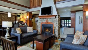 A cozy lobby with a stone fireplace, comfortable seating, a flat-screen TV, and a coffee station.