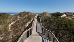 Een houten looppad naar het strand, omringd door duinen en begroeiing.