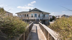 Een huis aan het strand met een houten terras dat leidt naar een overdekte veranda.
