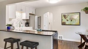 A kitchen with white cabinets, a stainless steel refrigerator, and a bar area with stools. - Walk to Falls / Close to Everything / Fenced Backyard (Minneapolis)