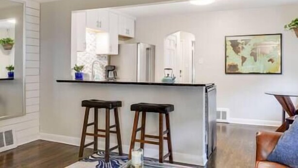 A modern kitchen with white cabinets, a black countertop, and two wooden stools. - Walk to Falls / Close to Everything / Fenced Backyard (Minneapolis)