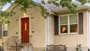 A single-story house with a red door, a front porch with a bench, and a small garden area. - Walk to Falls / Close to Everything / Fenced Backyard (Minneapolis)