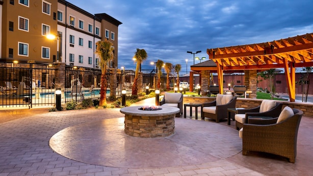 An outdoor patio area with a stone fire pit, wicker furniture, and a pool in the background. - King Suite | Access to Free Breakfast + Shared Pool & Hot Tub. Your Next Vacation! (St George)