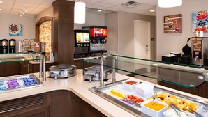 Zona de buffet con varios recipientes de comida, una estación de café y una máquina de Coca-Cola.