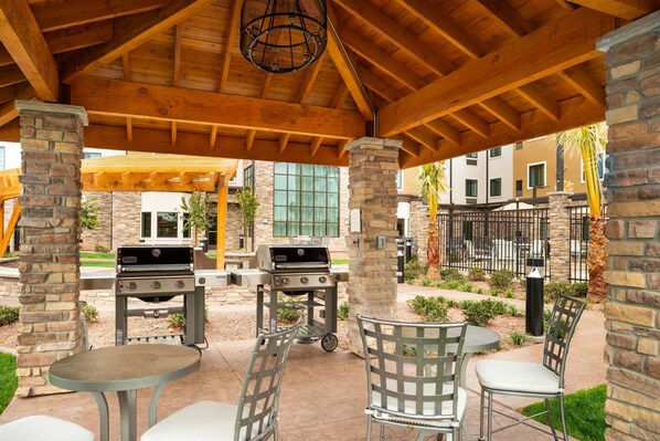 Enjoy dining and socializing in this outdoor patio area with a covered structure, round table, and barbecue grills.