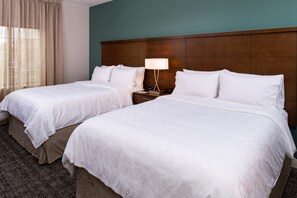 Ein Hotelzimmer mit zwei Betten, einem hölzernen Kopfteil, einem Nachttisch mit Lampe und einem Fenster mit durchsichtigen Vorhängen.