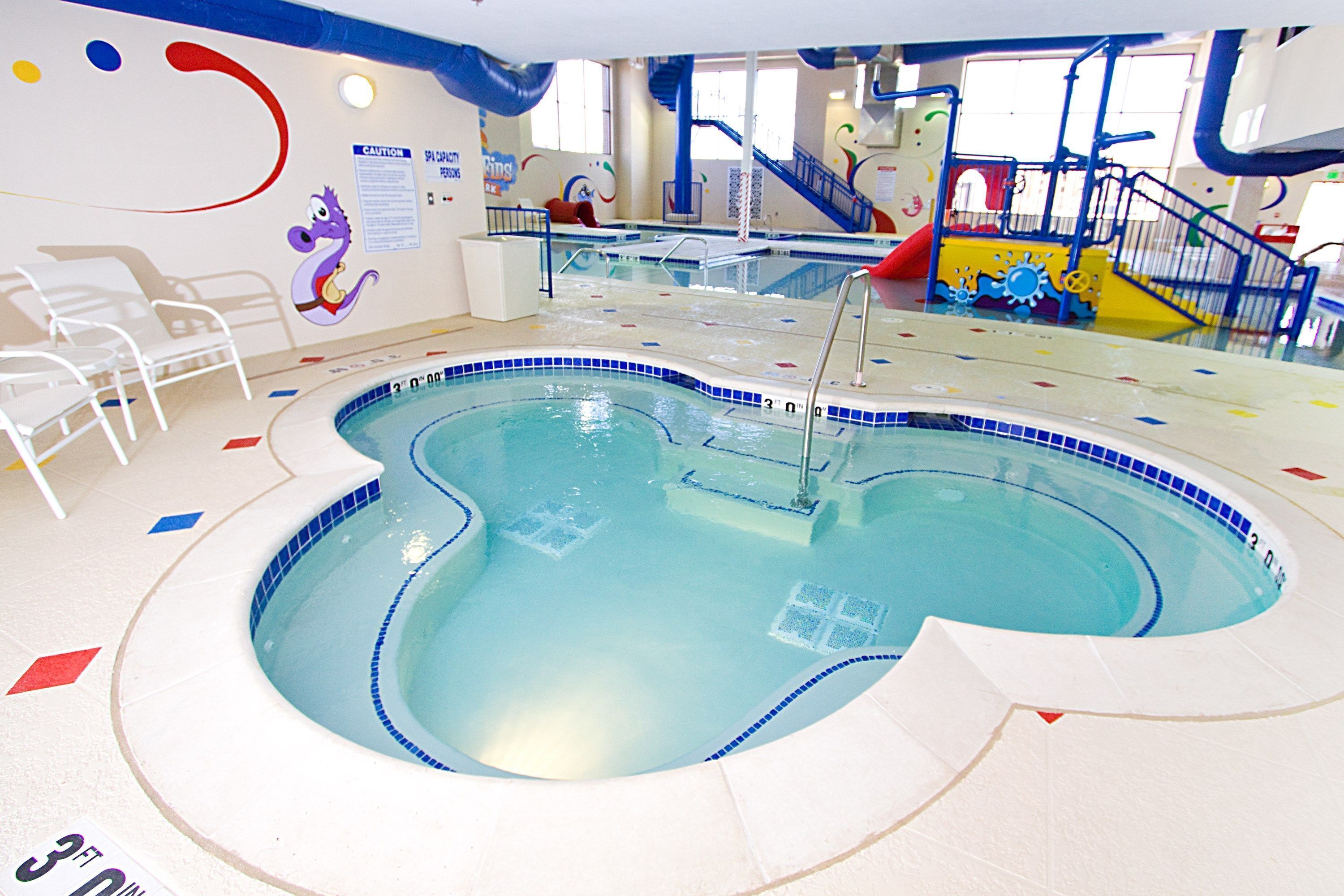 Una piscina interior con borde de azulejos azules y blancos, una escalera y un tobogán.