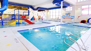 An indoor swimming pool with a slide, a water play area, and a sign for Grin & Fins Water Park.