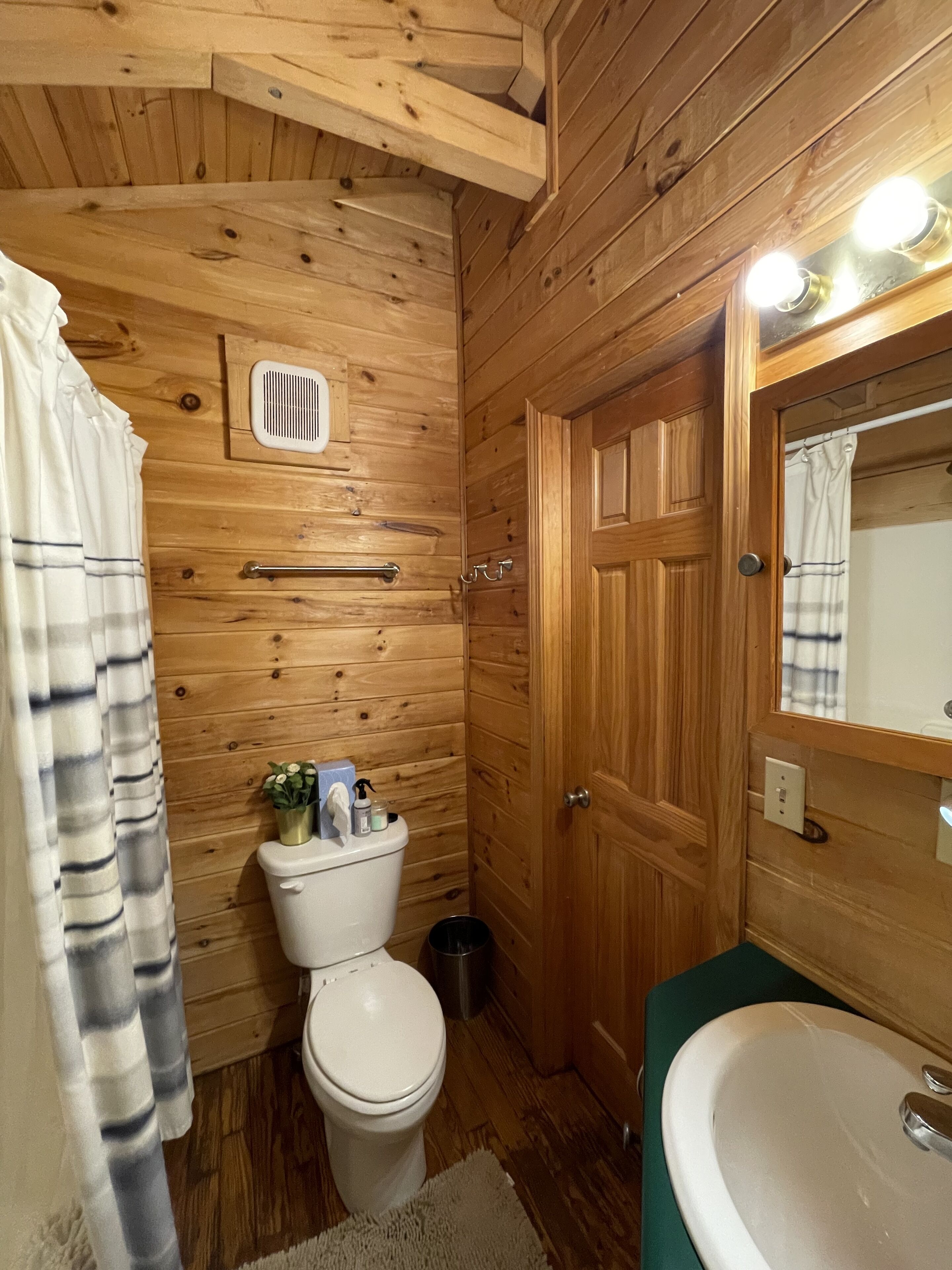 A wooden-paneled bathroom with a toilet, a sink, and a shower curtain.