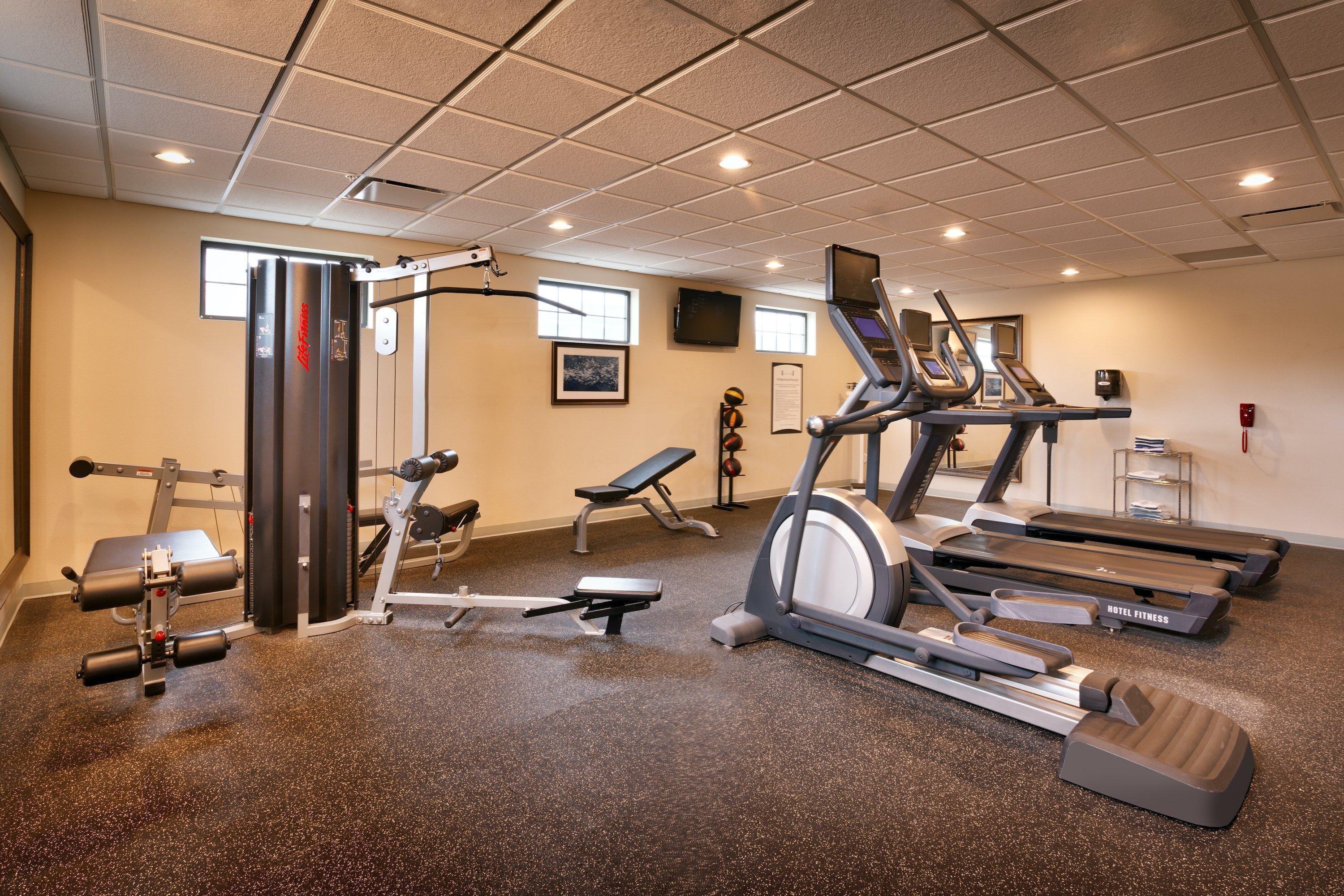Een hotel fitnessruimte met loopbanden, krachtapparaten en een tv aan de muur.