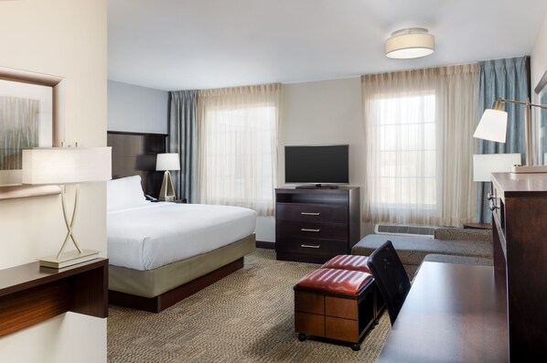 A hotel room with a bed, a desk, a television, a dresser, and a lamp.