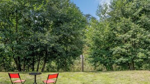 Zona exterior amb gespa, amb dues cadires vermelles i una taula petita, envoltada per arbres densos.