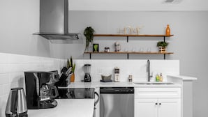 A modern kitchen with white cabinets, stainless steel appliances, and wooden shelves with decorative items. - Amazing Blue Private Pool - 4BR House Near Disney (Kissimmee)
