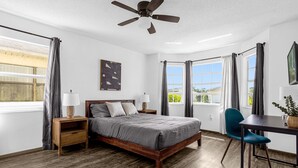 A bedroom with a wooden bed, a desk with a chair, a ceiling fan, and large windows with curtains. - Amazing Blue Private Pool - 4BR House Near Disney (Kissimmee)