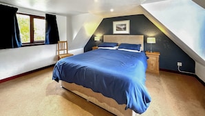 Ein Schlafzimmer mit einem großen Bett, einem Sessel, einem Nachttisch und einem Fenster mit Vorhängen.