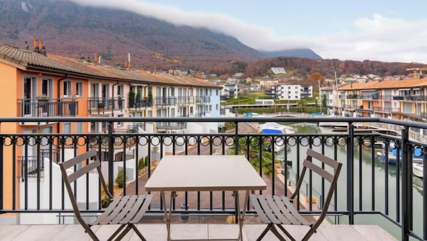 Ein Balkon mit Tisch und zwei Stühlen, mit Blick auf eine Stadt, Gebäude und einen Berg im Hintergrund.