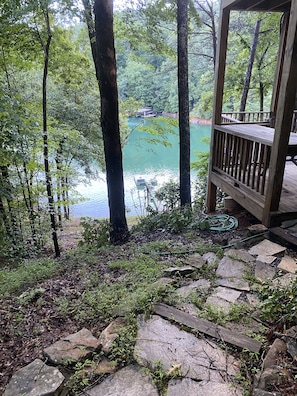 Overlooking a serene lake, this deck offers a peaceful retreat surrounded by lush greenery and tall trees.