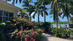 Un sentier menant à un bâtiment d’où l’on peut admirer la mer, le tout étant entouré de palmiers et de plantes en fleurs.