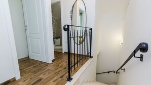 Una escalera con barandilla de metal negro, paredes blancas y suelo de madera.